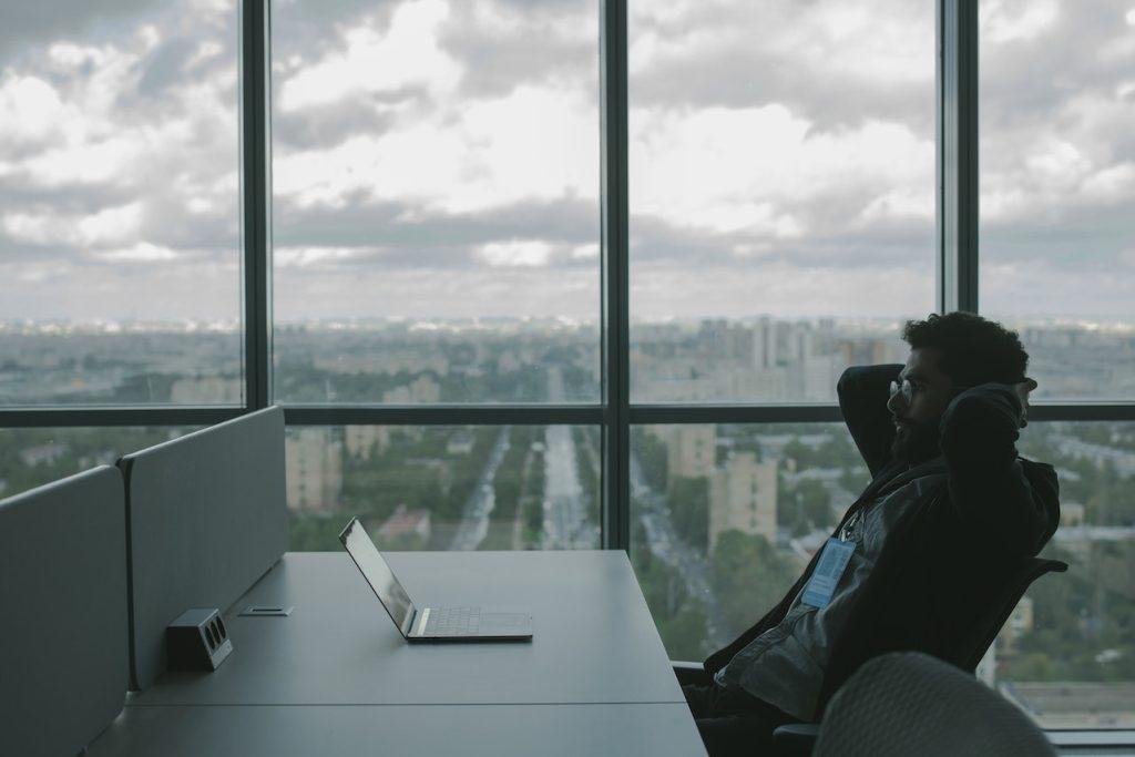 Man leaning back in front of a laptop with a clear view of a city