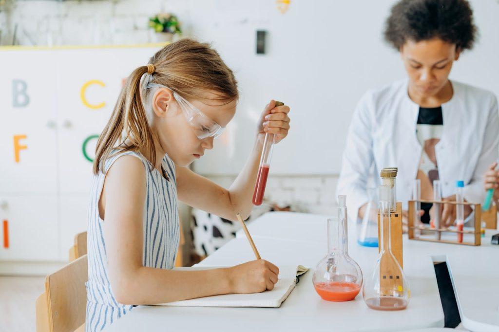 A Girl Holding a Test Tube While Writing in a Notebook