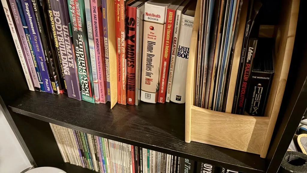 Various bodybuilding and fitness books and magazines in a bookcase.